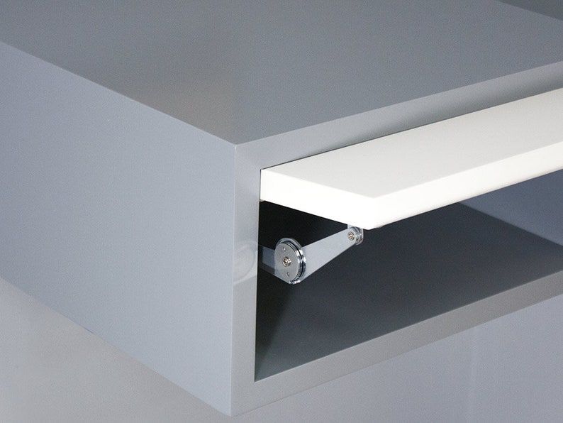 May include: A gray cabinet with a white shelf that is partially open. The shelf is attached to the cabinet with a silver hinge.