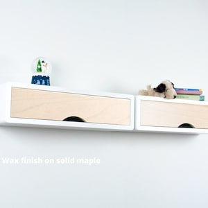 May include: White wall-mounted shelf with two drawers. The drawers are made of solid maple wood with a wax finish. The shelf is decorated with a snow globe and a stuffed animal.