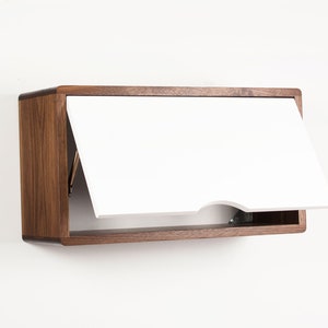 May include: A wall-mounted cabinet with a white door that opens upwards. The cabinet is made of wood with a dark brown finish.