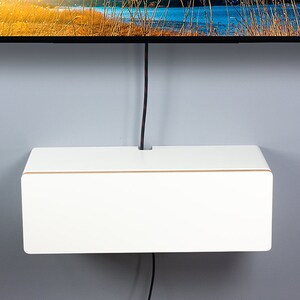May include: White wall-mounted shelf with a brown trim, designed to conceal cords and wires. The shelf is mounted below a flat screen television.