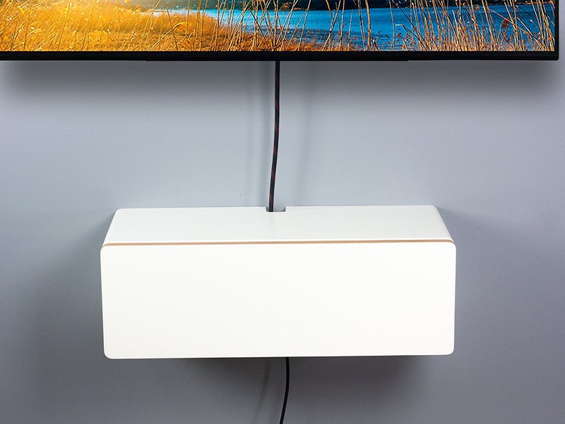 May include: White wall-mounted shelf with a brown trim, designed to conceal cords and wires. The shelf is mounted below a flat screen television.