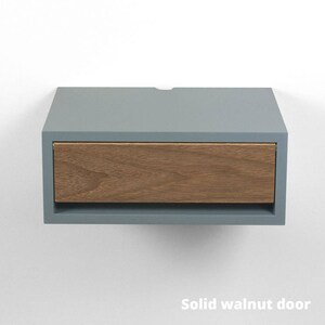 May include: A light blue floating nightstand with a single drawer made of solid walnut wood. The drawer is open and the wood grain is visible.