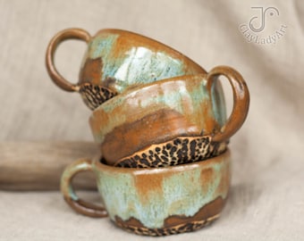 May include: Three stacked ceramic mugs with a brown, green and white glaze. The mugs have a speckled pattern and a unique, handmade look.