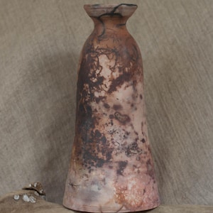 Può includere: Un vaso in ceramica fatto a mano con un design organico unico. Il vaso presenta una base svasata e un collo stretto, con una superficie screziata nei toni del marrone, beige e rosa-rossastro. Il vaso è alto circa 25 cm.