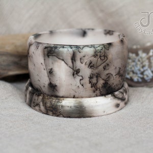 May include: A set of two ceramic bracelets with a white base and black swirling patterns. The bracelets are stacked on top of each other.