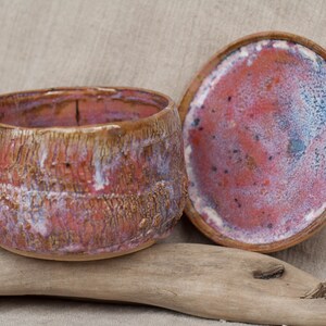 May include: A ceramic bowl with a lid, both with a red, white, and brown glaze. The bowl has a textured surface and the lid has a smooth surface.
