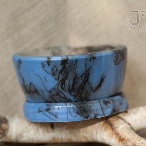 May include: A small blue ceramic planter with a black and white abstract design. The planter has a wide rim and a slightly flared base.