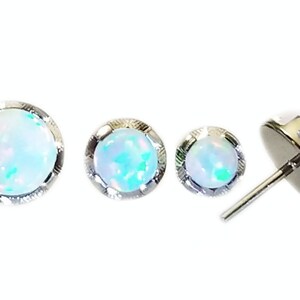 May include: Three silver stud earrings with white opal stones. The stones have a slight iridescent green hue.
