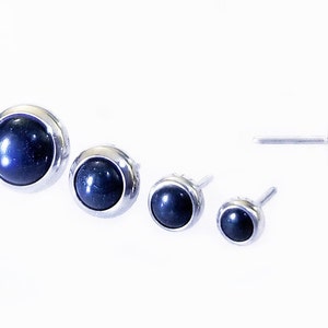 May include: Set of four silver stud earrings with black gemstone accents. The earrings are different sizes.