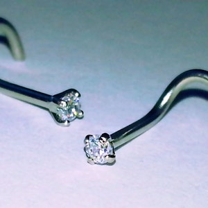 May include: Two silver nose rings with clear crystal stones. The rings are curved and have a small, round stone at the end.