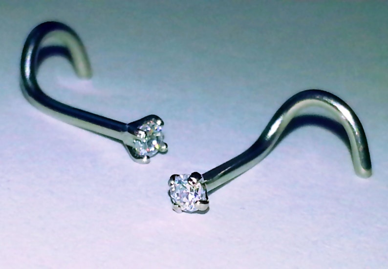 May include: Two silver nose rings with clear crystal stones. The rings are curved and have a small, round stone at the end.