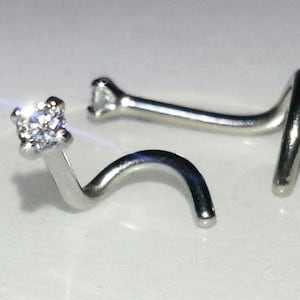 May include: A silver nose ring with a clear cubic zirconia stone. The ring is curved and has a small ball at the end.
