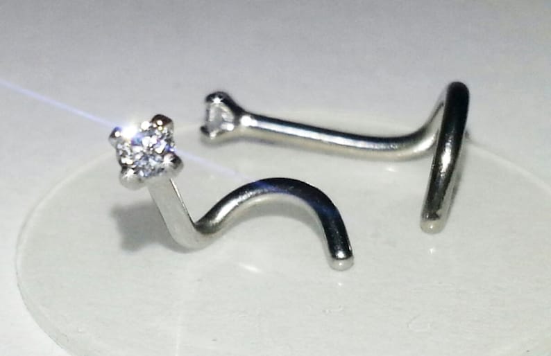 May include: A silver nose ring with a clear cubic zirconia stone. The ring is curved and has a small ball at the end.