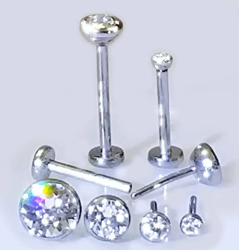 May include: A set of six silver body jewelry pieces with clear crystal accents. The jewelry includes a variety of sizes and styles, including a labret stud, a nose ring, and a lip ring.
