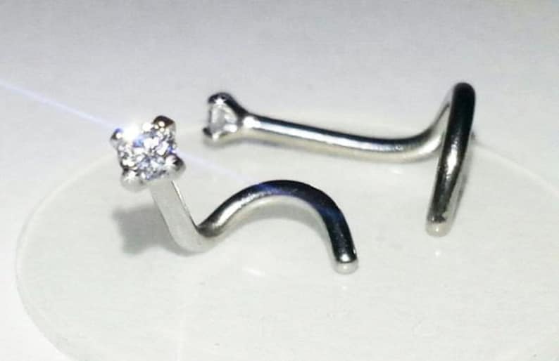 May include: Two silver nose rings with a clear gemstone on one end. The rings are curved and have a small loop on the other end.