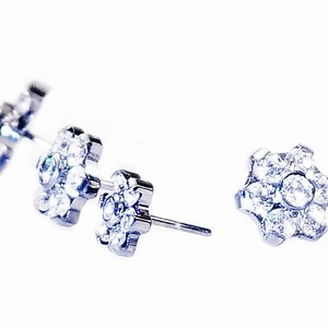 K&ouml;nnte beinhalten: Ein Paar silberne Ohrstecker mit Blumenmuster. Jede Blume besteht aus kleinen, klaren Strasssteinen.