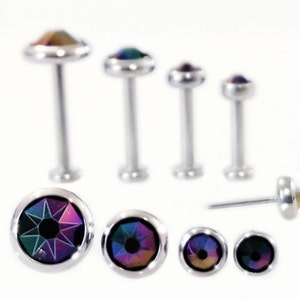 May include: A set of seven silver body jewelry pieces with iridescent rainbow colored gems. The set includes five barbell style pieces with different lengths and one stud style piece. The gems are round and have a faceted design.