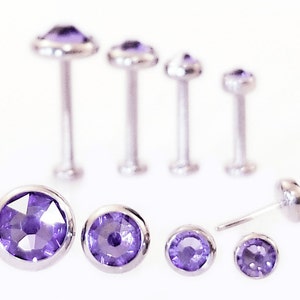May include: A set of six silver body jewelry pieces with purple gemstones. The jewelry is in various sizes and styles, including studs and barbells.