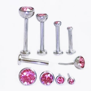 May include: A set of six surgical steel body jewelry pieces with pink gem stones. The pieces are different sizes and styles, including labret studs, nose rings, and lip rings.