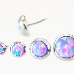 May include: Four opal stud earrings in varying sizes. Each earring features a round, iridescent opal stone set in a silver-colored bezel. One earring is shown from the side, displaying the post. The opals display shades of pink, blue, and green.