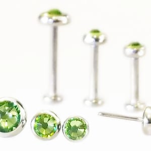 May include: Four silver nose rings with green gem stones. The rings are different sizes.