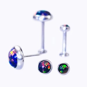 May include: Three silver body jewelry pieces with iridescent opal stones. The largest piece is a barbell with a 5mm opal stone. The other two pieces are studs with 4mm opal stones.