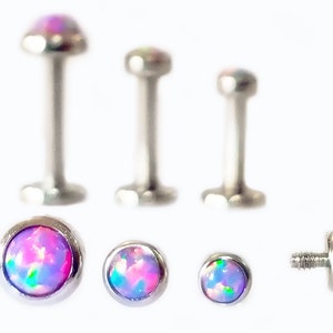 May include: A set of seven surgical steel body jewelry pieces with opal-like gemstones in shades of pink, purple, and green. The set includes three barbell posts in different lengths and four flat-back studs in different sizes.