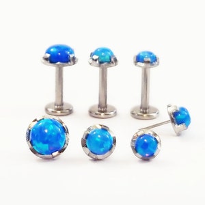 May include: Six surgical steel body jewelry pieces with blue opal gemstones. Three are barbell style with a post and a ball on each end. Three are studs with a post and a single ball.