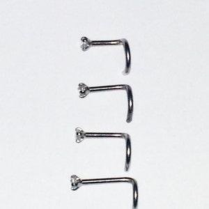 May include: Four silver nose rings with a small clear gemstone on the end of each ring.