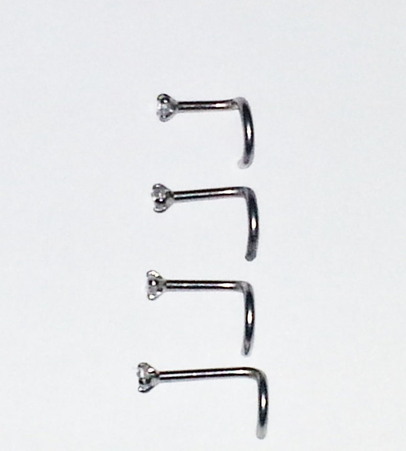 May include: Four silver nose rings with a small clear gemstone on the end of each ring.