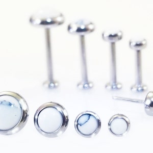 May include: A set of six silver body jewelry pieces with white stone tops. The stones have a marbled pattern. The jewelry is in various sizes.