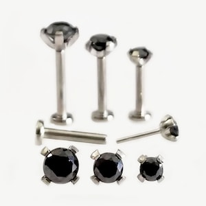 May include: A collection of black gemstone labret studs and posts in various sizes. The jewelry features a silver-colored metal setting and a round, black gemstone. The studs are designed for lip or ear piercings.