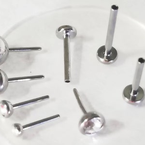 May include: A set of six silver nose rings with clear crystal stones. The rings are different sizes and styles, including a straight post with a ball end, a curved post with a ball end, and a straight post with a crystal stone.