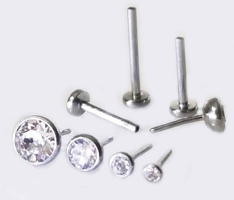 May include: A set of six silver body jewelry pieces with clear crystal accents. The jewelry includes two labret studs, two nose rings, and two small stud earrings.