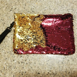 Puede incluir: Clutch rectangular de lentejuelas con una correa de mu&ntilde;eca negra. El clutch est&aacute; dividido en dos secciones: una mitad dorada y la otra burdeos. Las lentejuelas son peque&ntilde;as y redondas, creando un efecto brillante.