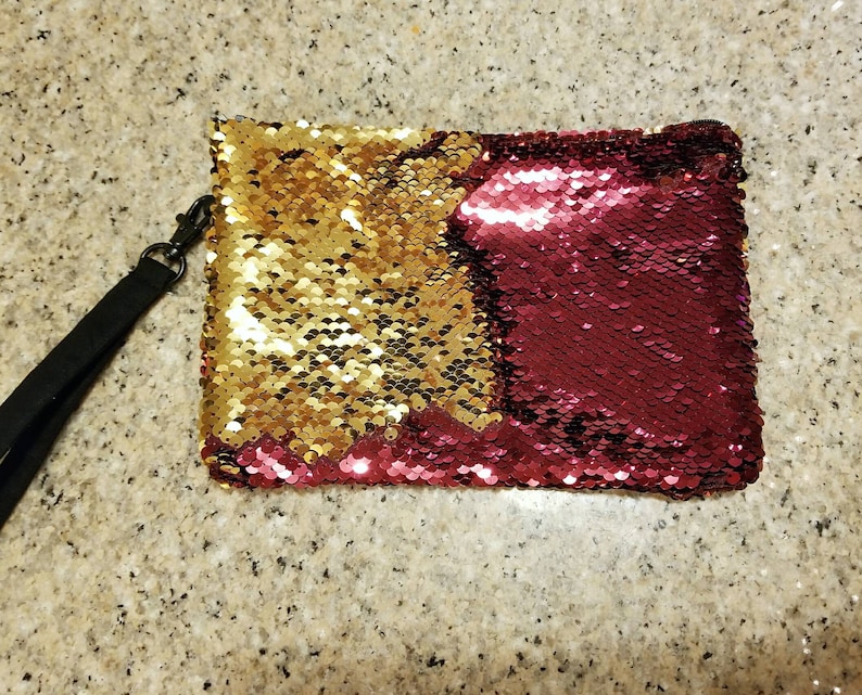 Puede incluir: Clutch rectangular de lentejuelas con una correa de mu&ntilde;eca negra. El clutch est&aacute; dividido en dos secciones: una mitad dorada y la otra burdeos. Las lentejuelas son peque&ntilde;as y redondas, creando un efecto brillante.