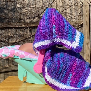 May include: A purple, blue, and white crocheted baby blanket with a white border. The blanket is draped over a pink and white polka dot car seat.