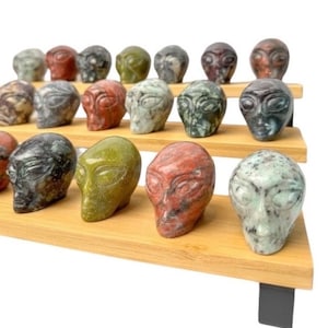 May include: A collection of 20 small, carved alien head sculptures made of various types of green, red, and black stone. The sculptures are displayed on a three-tiered bamboo shelf with black metal brackets.