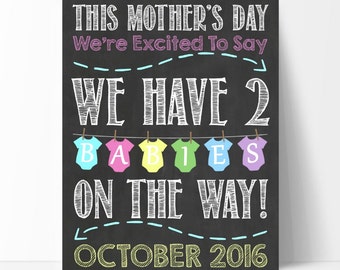 May include: Chalkboard style announcement for Mother's Day. It says "This Mother's Day We're Excited To Say We Have 2 Babies On The Way! October 2016". The text is in white and the background is black. There are colorful baby onesies hanging on a clothesline above the text.