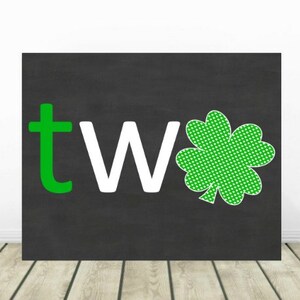 May include: A black chalkboard with the word "two" written in green and white letters. A green shamrock with white polka dots is to the right of the word.