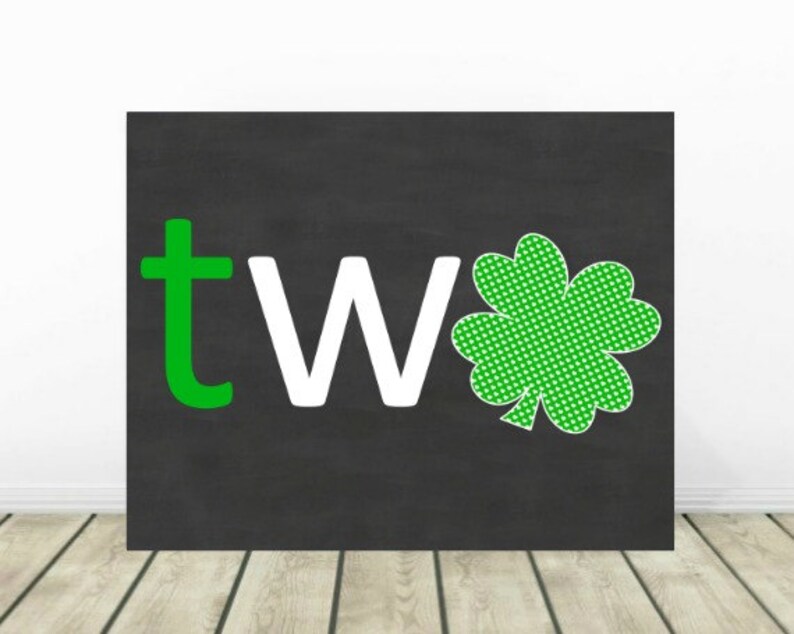 May include: A black chalkboard with the word "two" written in green and white letters. A green shamrock with white polka dots is to the right of the word.