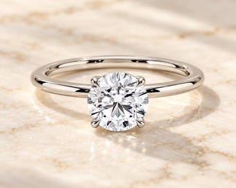 May include: A silver-toned ring featuring a single, round, brilliant-cut clear stone set in a four-prong setting. The band is smooth, polished, and circular, showcasing a reflective metallic finish that catches the light.