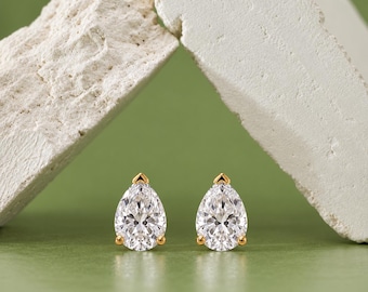 May include: A pair of pear-shaped stud earrings featuring clear, faceted stones set in gold-toned metal. Each earring is secured with a small, pointed gold-toned prong at the top and two additional prongs at the base, creating a classic, elegant look.