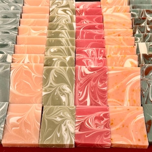 May include: A tray of handmade soap bars in three different colors and patterns: green with white swirls, pink with white swirls, and orange with white swirls.