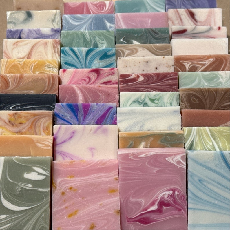 May include: A collection of 25 handmade soap bars with various colors and swirl patterns. The soap bars are arranged in rows and columns, creating a visually appealing display.