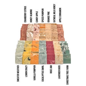 May include: A display of 14 different handcrafted soap bars with various colors and patterns. The soap bars are arranged in a staggered pattern, with the names of each scent printed below.