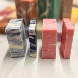 May include: Four bars of handmade soap, two are blue and white marbled, one is pink marbled, and one is a dark blue and white marbled.