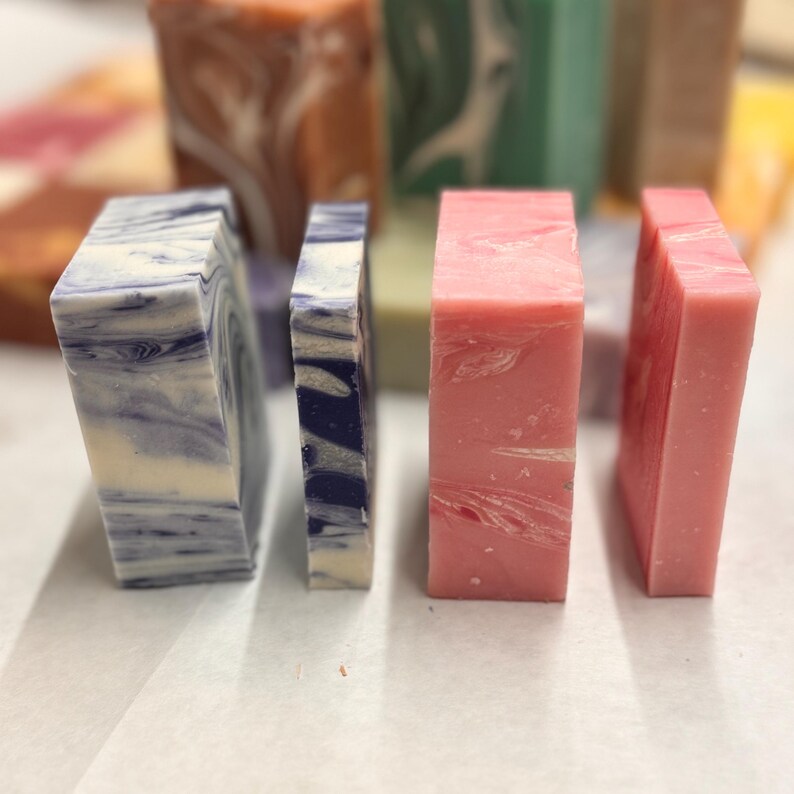 May include: Four bars of handmade soap, two are blue and white marbled, one is pink marbled, and one is a dark blue and white marbled.
