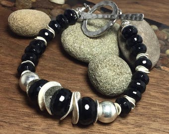 May include: A black onyx and silver bracelet with a toggle clasp. The bracelet features faceted black onyx beads and silver spacer beads.
