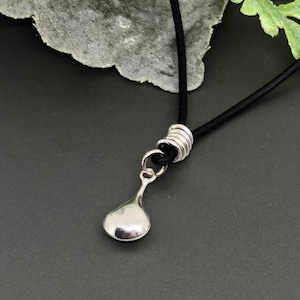 May include: A silver teardrop pendant necklace with a black cord. The pendant is attached to the cord with a silver ring.